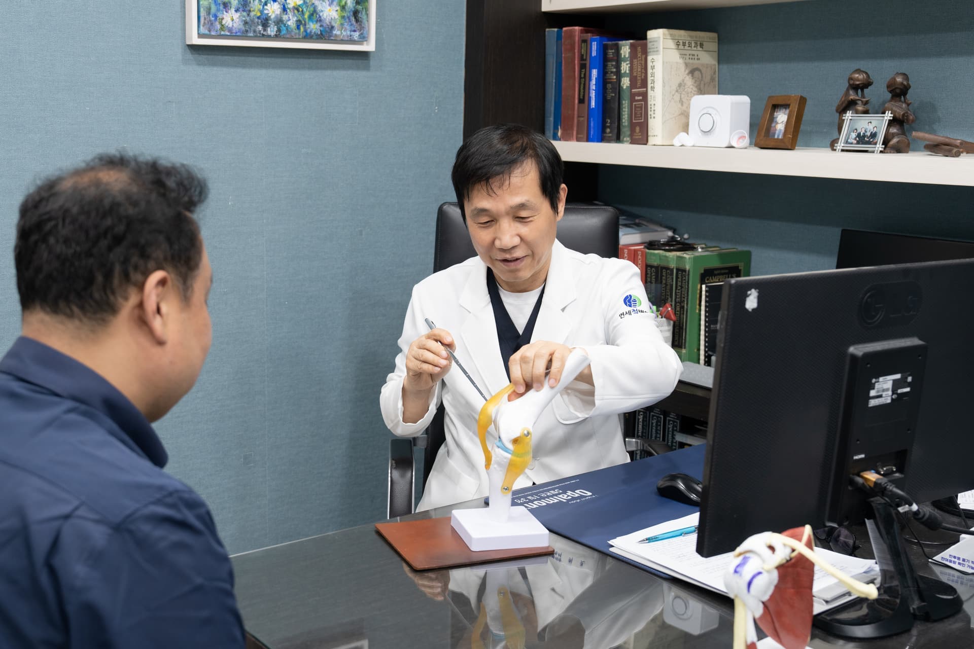 연세척병원 의료진이 무릎 관절 모형으로 환자에게 관절 상태를 설명하는 진료 장면